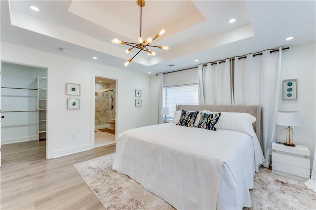 bedroom with a closet, a spacious closet, light hardwood / wood-style floors, a tray ceiling, and ensuite bathroom