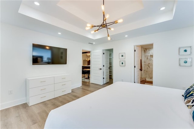 bedroom with light hardwood / wood-style flooring, a raised ceiling, and ensuite bath