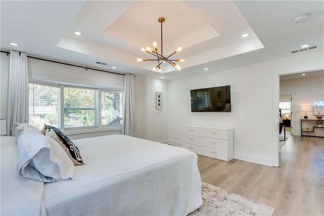 bedroom with light wood-type flooring, a tray ceiling, and an inviting chandelier