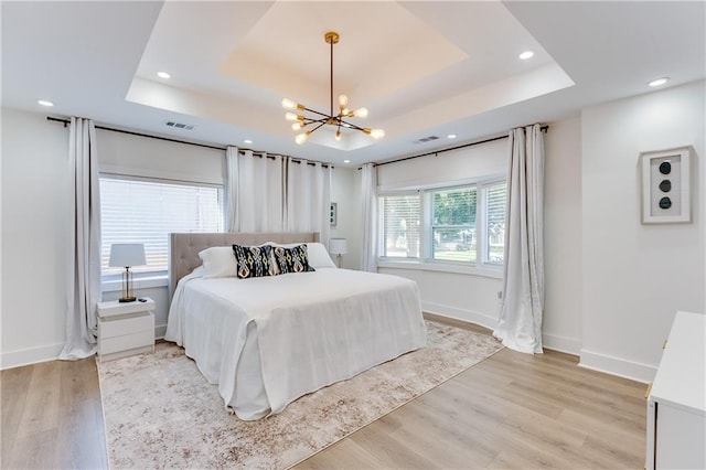 bedroom with a raised ceiling, light wood-type flooring, and a notable chandelier