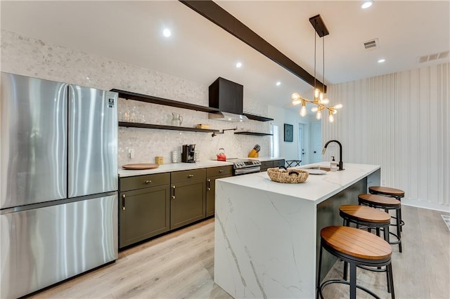 kitchen with sink, a kitchen island with sink, stainless steel refrigerator, pendant lighting, and light wood-type flooring