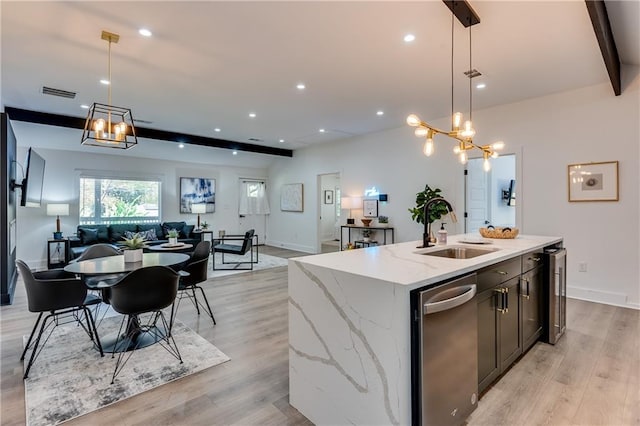 kitchen with sink, beam ceiling, hanging light fixtures, a kitchen island with sink, and light hardwood / wood-style flooring