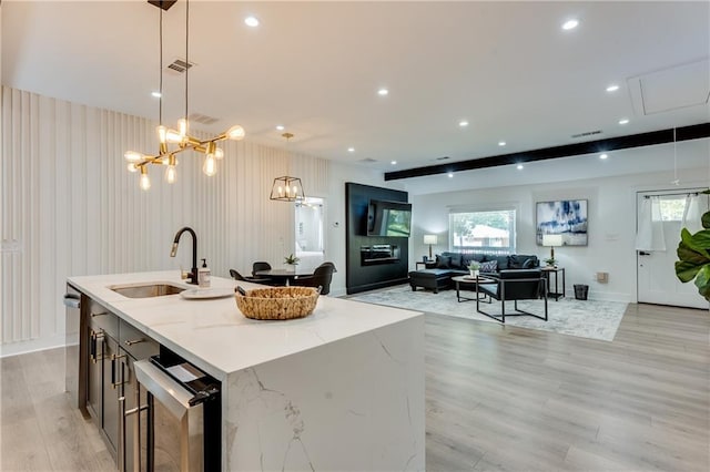 kitchen with a center island with sink, light stone countertops, pendant lighting, sink, and light hardwood / wood-style flooring