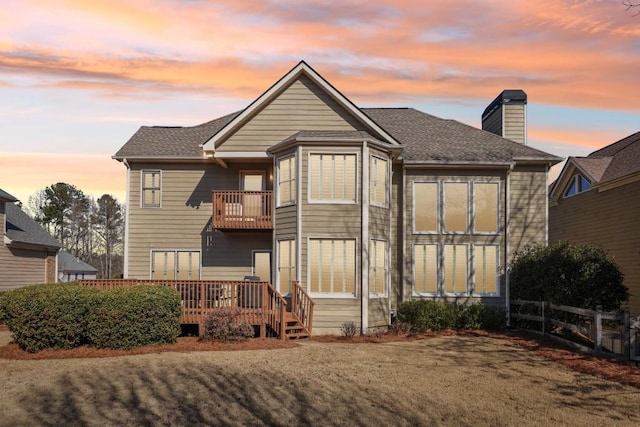 back house at dusk featuring a wooden deck and a lawn