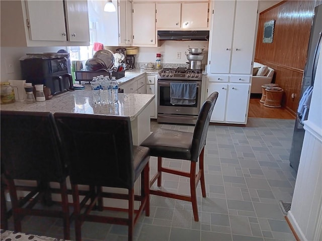 kitchen featuring a kitchen breakfast bar, white cabinets, kitchen peninsula, light stone counters, and stainless steel range with gas cooktop