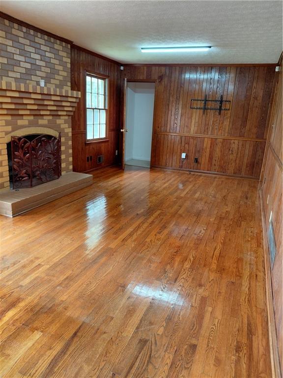 2479 Kingsland Dr, Dunwoody, GA 30360 - unfurnished living room with wood finished floors, wood walls, a brick fireplace, and a textured ceiling