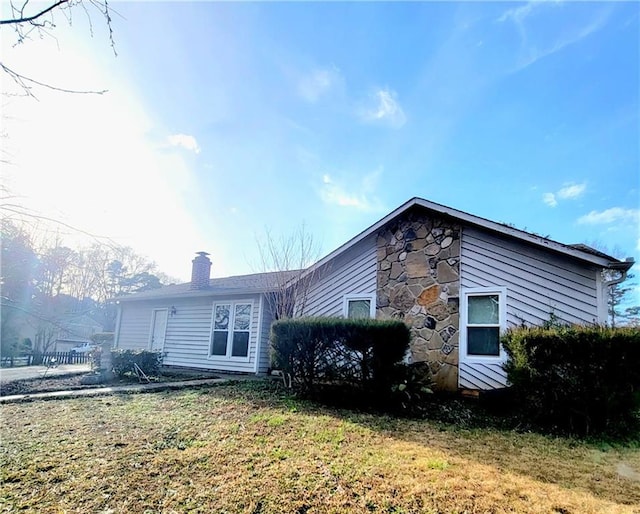 back of house featuring stone siding and a chimney