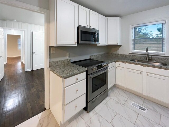 kitchen with appliances with stainless steel finishes, sink, dark stone counters, and white cabinets