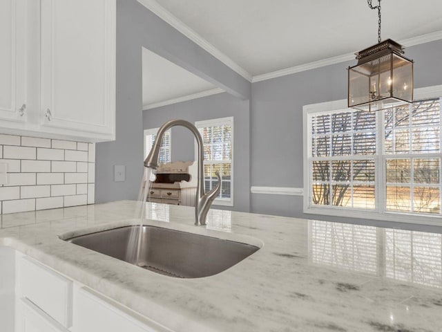kitchen with decorative backsplash, ornamental molding, light stone countertops, white cabinets, and a sink