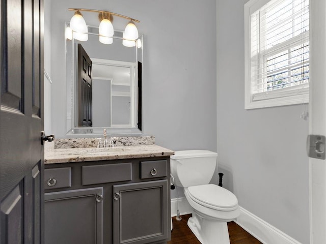 half bathroom with baseboards, vanity, toilet, and wood finished floors