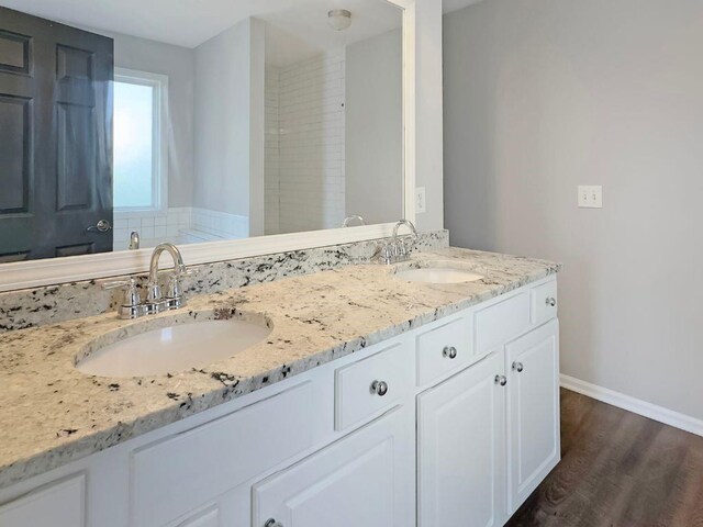 bathroom with double vanity, baseboards, a sink, and wood finished floors