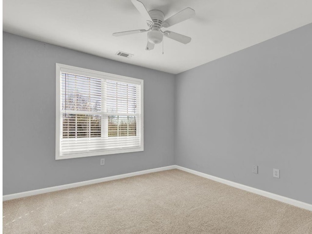 carpeted spare room with visible vents, baseboards, and ceiling fan