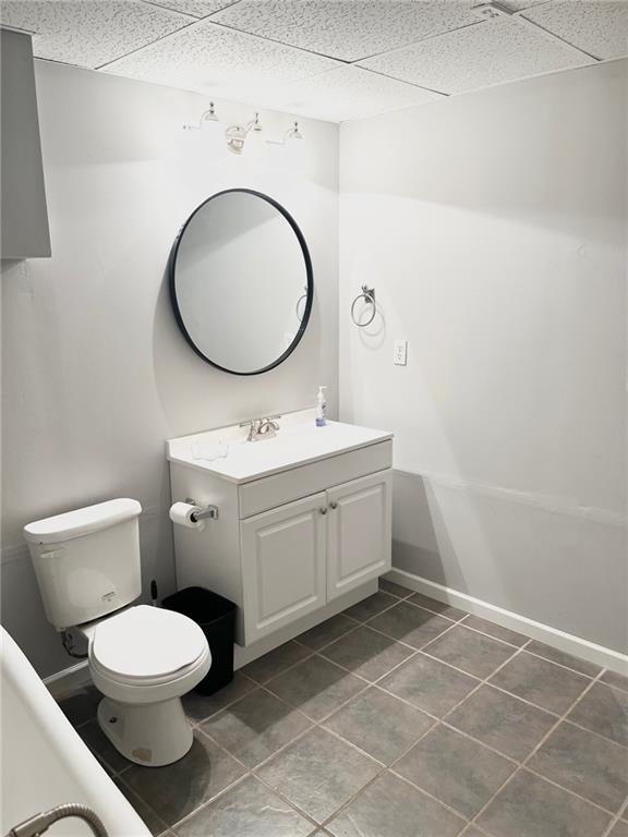 bathroom with tile patterned flooring, vanity, toilet, baseboards, and a paneled ceiling