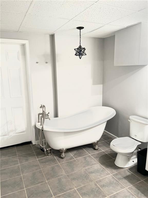 bathroom featuring tile patterned flooring, a paneled ceiling, toilet, and a soaking tub