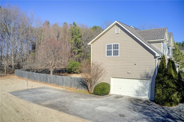 view of side of home with an attached garage, a shingled roof, and concrete driveway
