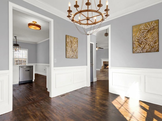 unfurnished dining area featuring crown molding, visible vents, a stone fireplace, a wainscoted wall, and dark wood finished floors
