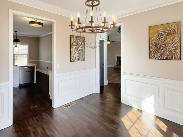 unfurnished dining area featuring crown molding, wainscoting, ceiling fan with notable chandelier, dark wood-type flooring, and visible vents