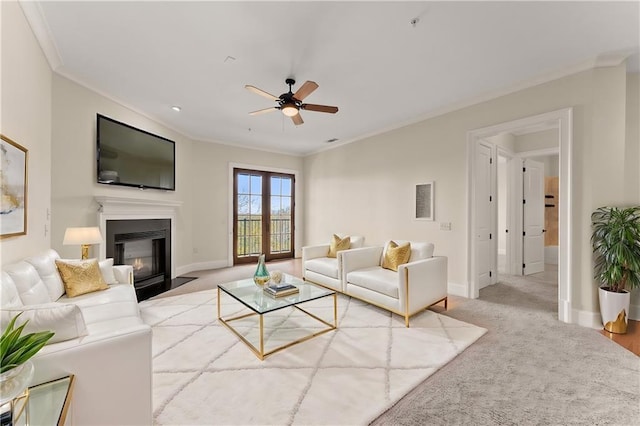 carpeted living area featuring a fireplace with flush hearth, ceiling fan, baseboards, and ornamental molding
