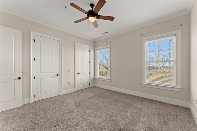 unfurnished bedroom featuring multiple closets, light colored carpet, ornamental molding, and ceiling fan