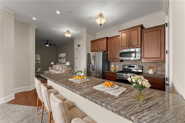 kitchen featuring tasteful backsplash, brown cabinets, stainless steel appliances, stone counters, and ornamental molding