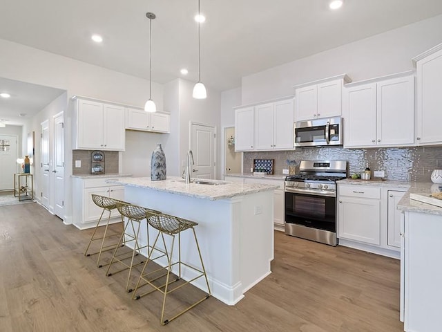 kitchen featuring a kitchen island with sink, stainless steel appliances, a sink, white cabinetry, and pendant lighting