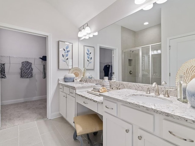 bathroom featuring double vanity, a stall shower, a walk in closet, and a sink