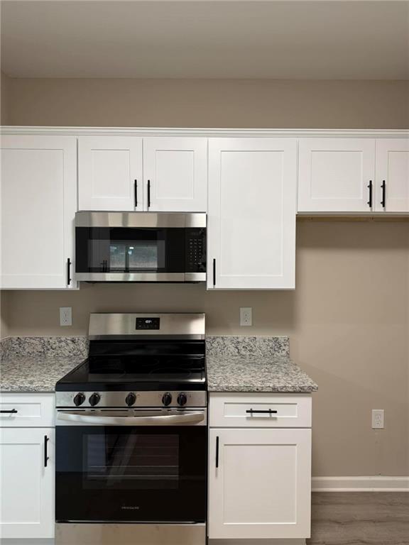 kitchen with light stone counters, white cabinetry, stainless steel appliances, and dark wood-type flooring