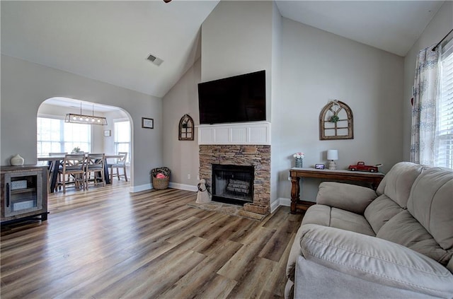 living room featuring a stone fireplace, wood-type flooring, and high vaulted ceiling