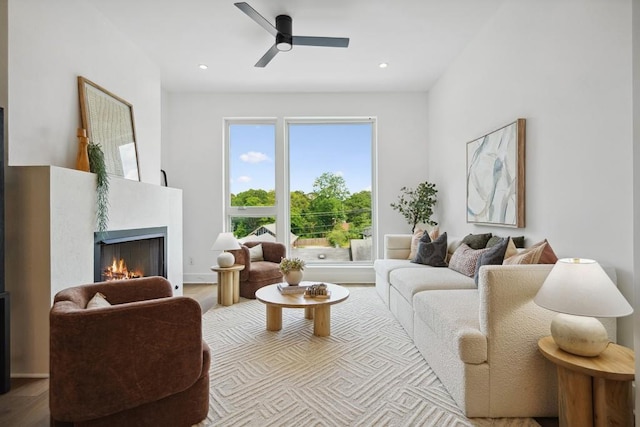 living room featuring recessed lighting, a warm lit fireplace, wood finished floors, and a ceiling fan
