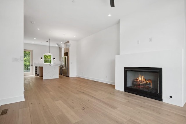 unfurnished living room with light wood-style flooring, visible vents, recessed lighting, ceiling fan, and a lit fireplace
