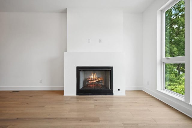 interior details featuring baseboards, a lit fireplace, and wood finished floors