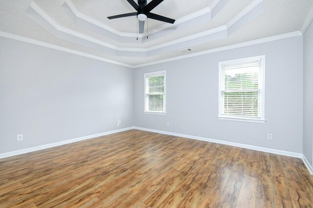 empty room with a tray ceiling, plenty of natural light, hardwood / wood-style floors, and crown molding