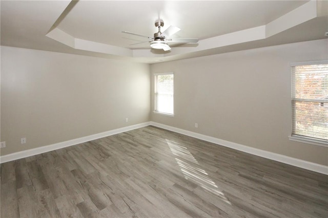 unfurnished room with ceiling fan, dark wood-type flooring, and a tray ceiling