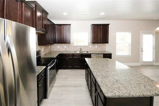 kitchen with decorative backsplash, light wood-type flooring, light stone counters, stainless steel appliances, and a center island