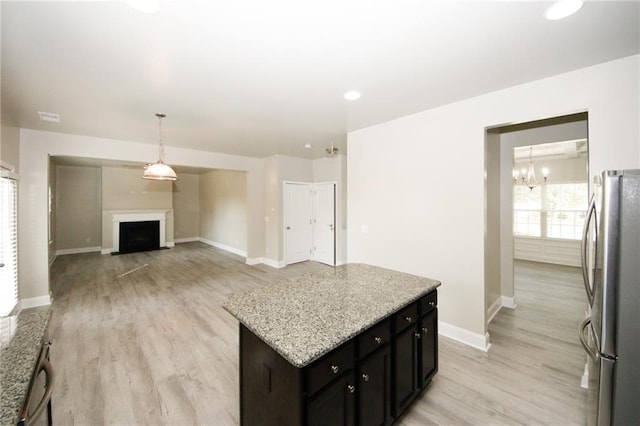 kitchen featuring a center island, light stone countertops, light wood-type flooring, a notable chandelier, and stainless steel refrigerator