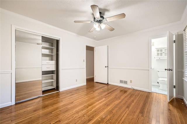 unfurnished bedroom featuring ornamental molding, ceiling fan, connected bathroom, wood-type flooring, and a closet