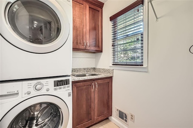 washroom with stacked washer and clothes dryer, light tile patterned floors, and cabinets