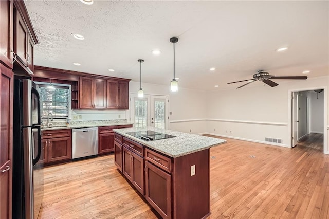 kitchen featuring stainless steel appliances, hanging light fixtures, light stone counters, a kitchen island, and sink