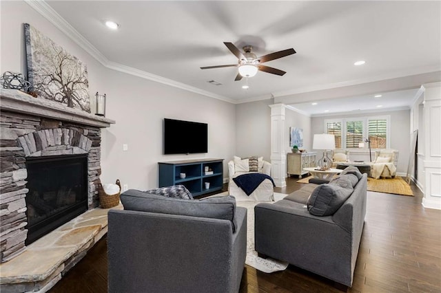 living room with a fireplace, a ceiling fan, dark wood finished floors, decorative columns, and crown molding