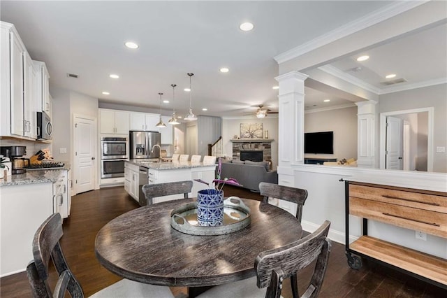 dining area with visible vents, ceiling fan, dark wood-type flooring, ornate columns, and a fireplace