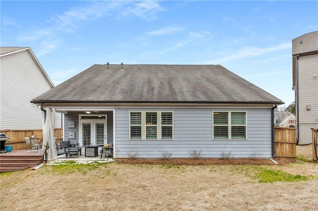 rear view of house featuring fence, roof with shingles, a lawn, a wooden deck, and a patio area