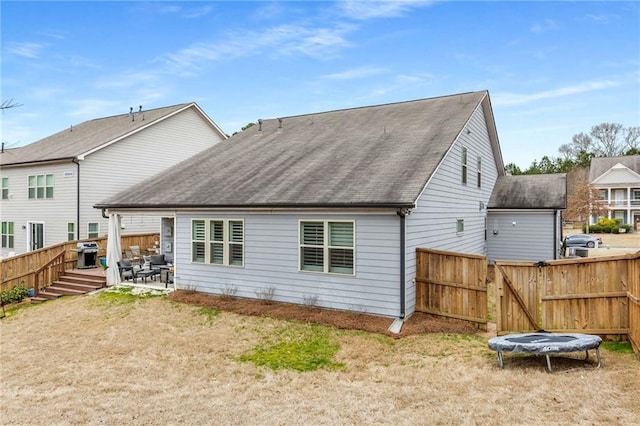 back of property featuring a patio, fence, roof with shingles, a gate, and a trampoline