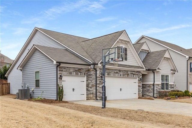 view of front of property featuring roof with shingles, central air condition unit, an attached garage, stone siding, and driveway