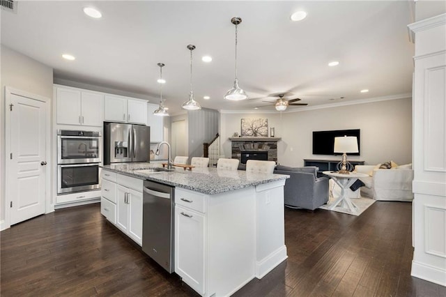 kitchen featuring a stone fireplace, dark wood-style flooring, a sink, appliances with stainless steel finishes, and decorative light fixtures