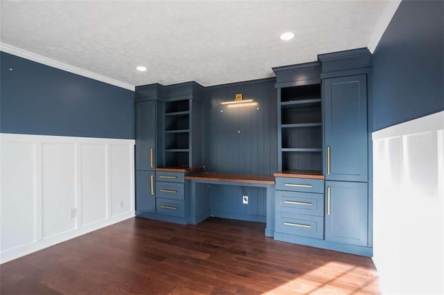 unfurnished office featuring dark wood-type flooring, a textured ceiling, ornamental molding, and built in desk