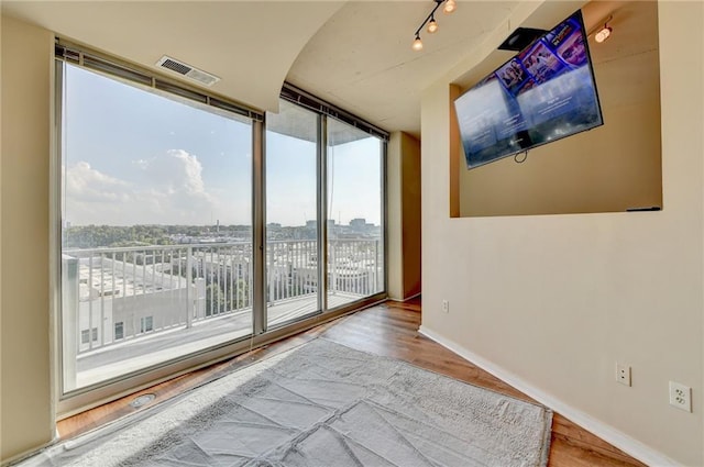 empty room featuring visible vents, baseboards, wood finished floors, and floor to ceiling windows