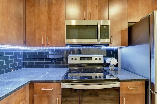 kitchen with dark countertops, brown cabinetry, appliances with stainless steel finishes, and decorative backsplash