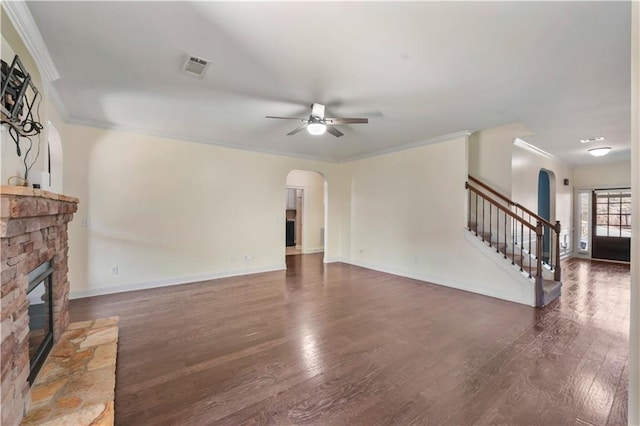 living room with arched walkways, a stone fireplace, stairs, and visible vents