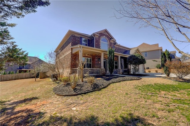 traditional home featuring a porch, brick siding, fence, and a front lawn