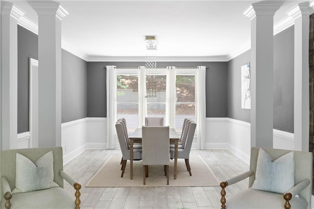 dining area featuring light hardwood / wood-style flooring, crown molding, and ornate columns